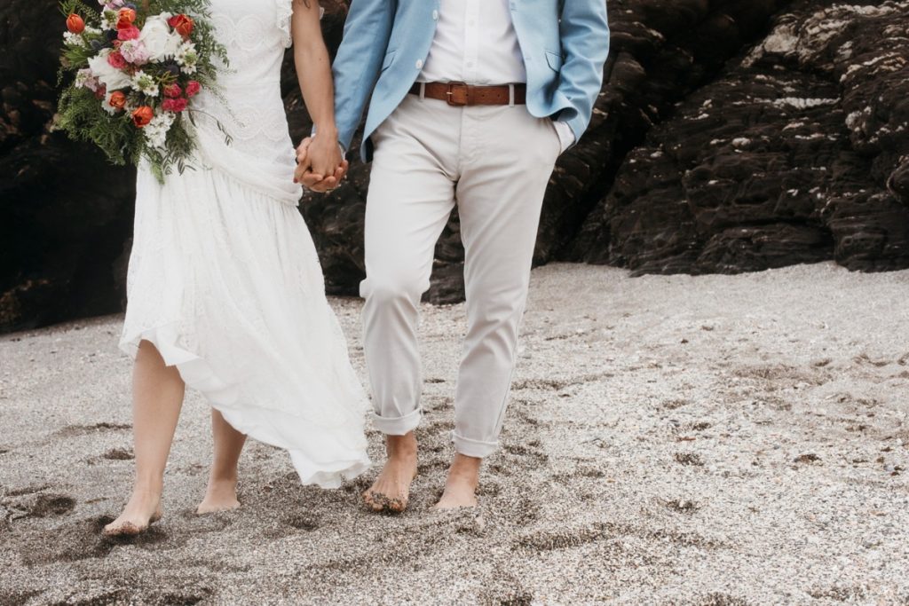 Couple walking barefoot on beach in wedding attire