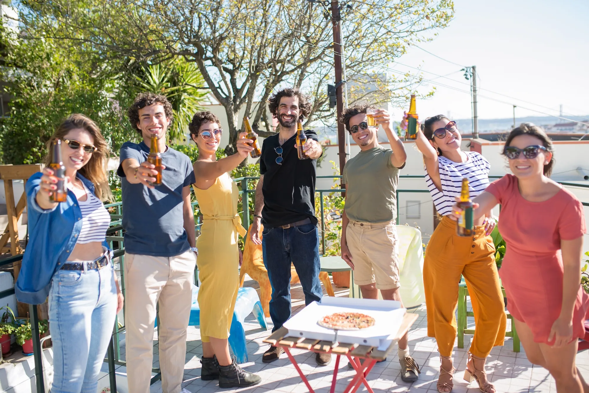 Friends toasting beers on sunny rooftop patio