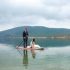 leonardo resenas whitelion Bride and groom paddleboarding on serene lake.